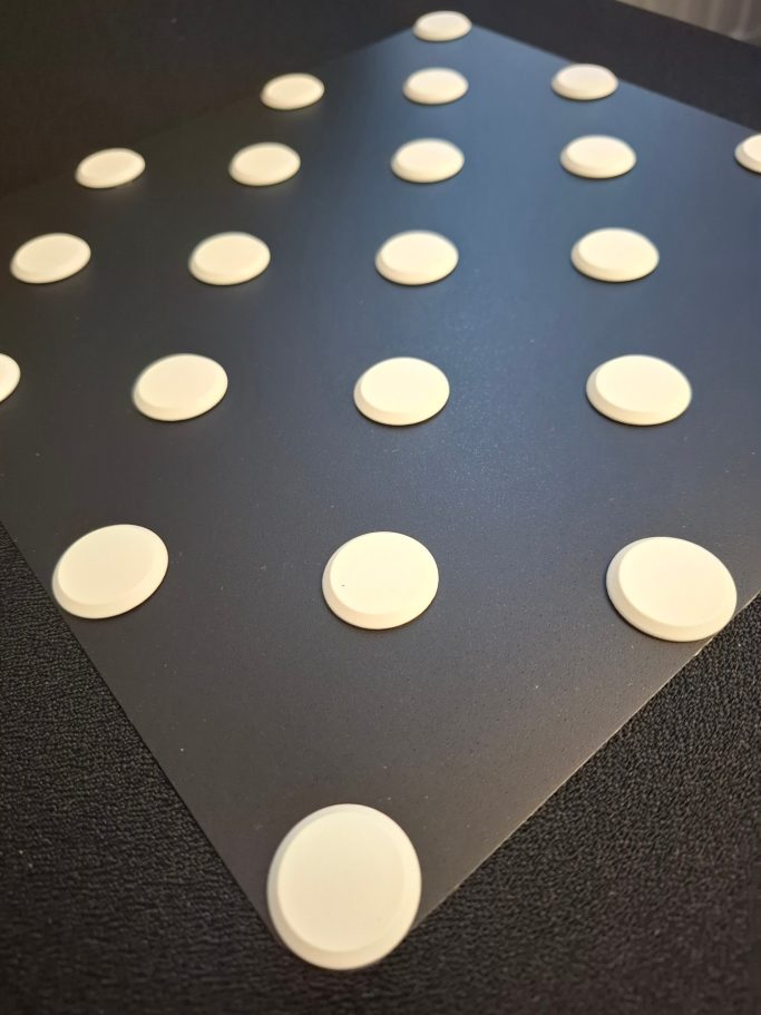 Ein schwarzer Untergrund mit mehreren weißen, runden Plättchen in gleichmäßigem Abstand.