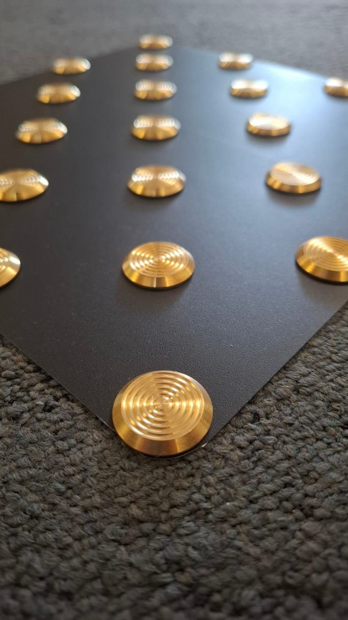 Schwarze Oberfläche mit goldenen, runden Noppen in regelmäßiger Anordnung.