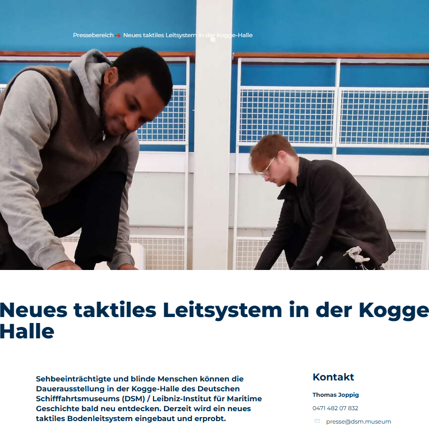 Zwei Männer installieren ein taktiles Leitsystem in der Kogge-Halle.